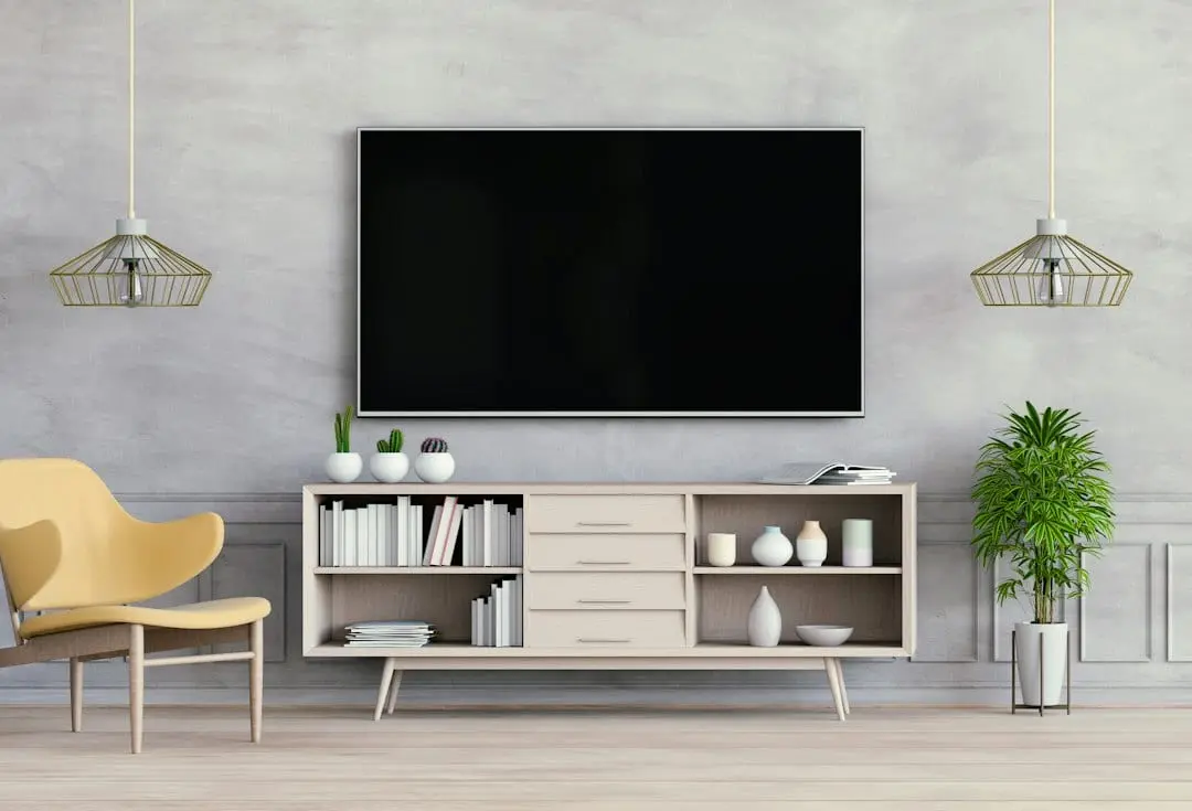 A large blank TV on a grey wall above a light wooden media unit with plants and books, the kind of screen for Flixaria in 4K