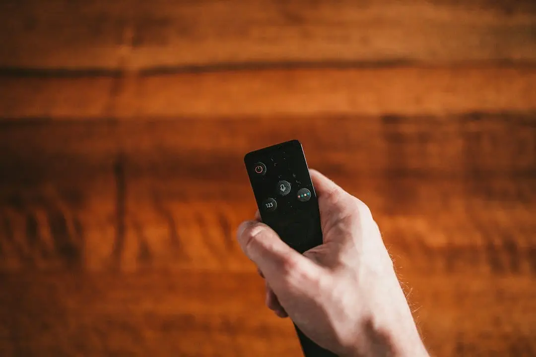 A hand holding a small black streaming remote over a wooden table, ready to set up Flixaria on a Fire TV Stick